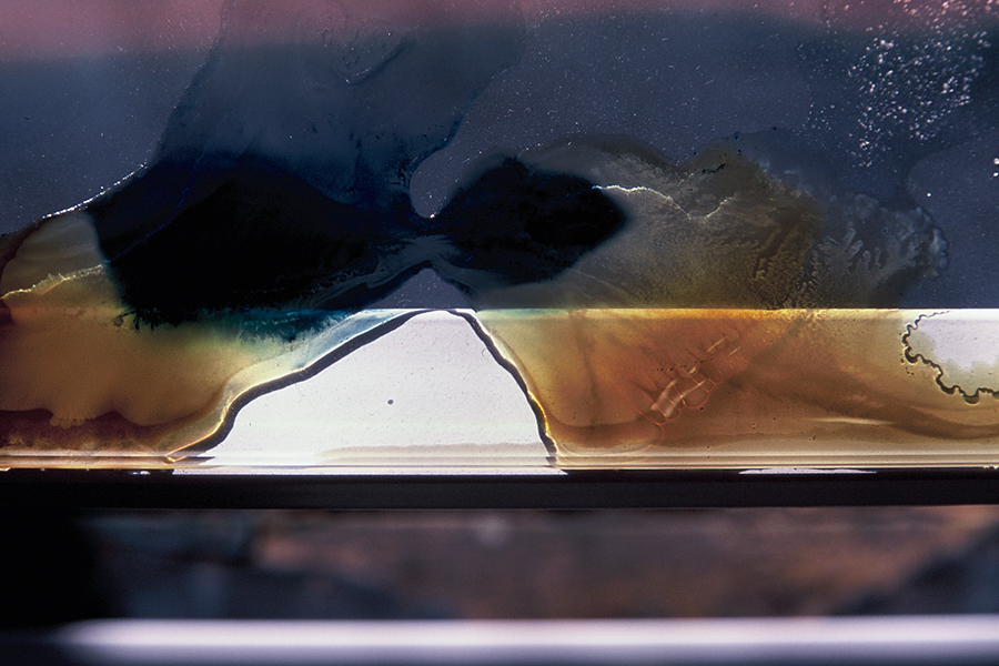 Close-up of blue, amber and translucent liquid forms on glass