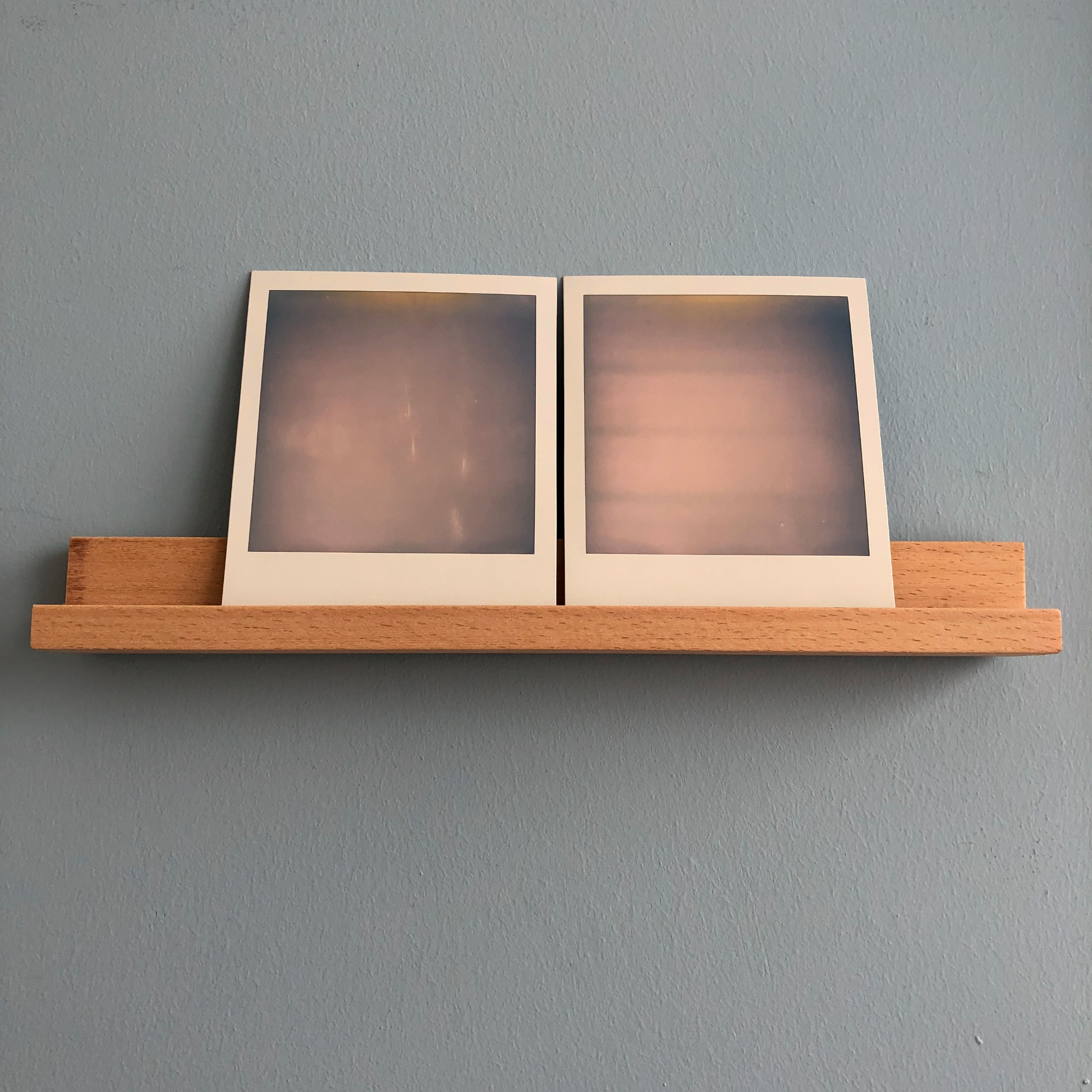 Two Polaroids presented together on a wooden shelf
